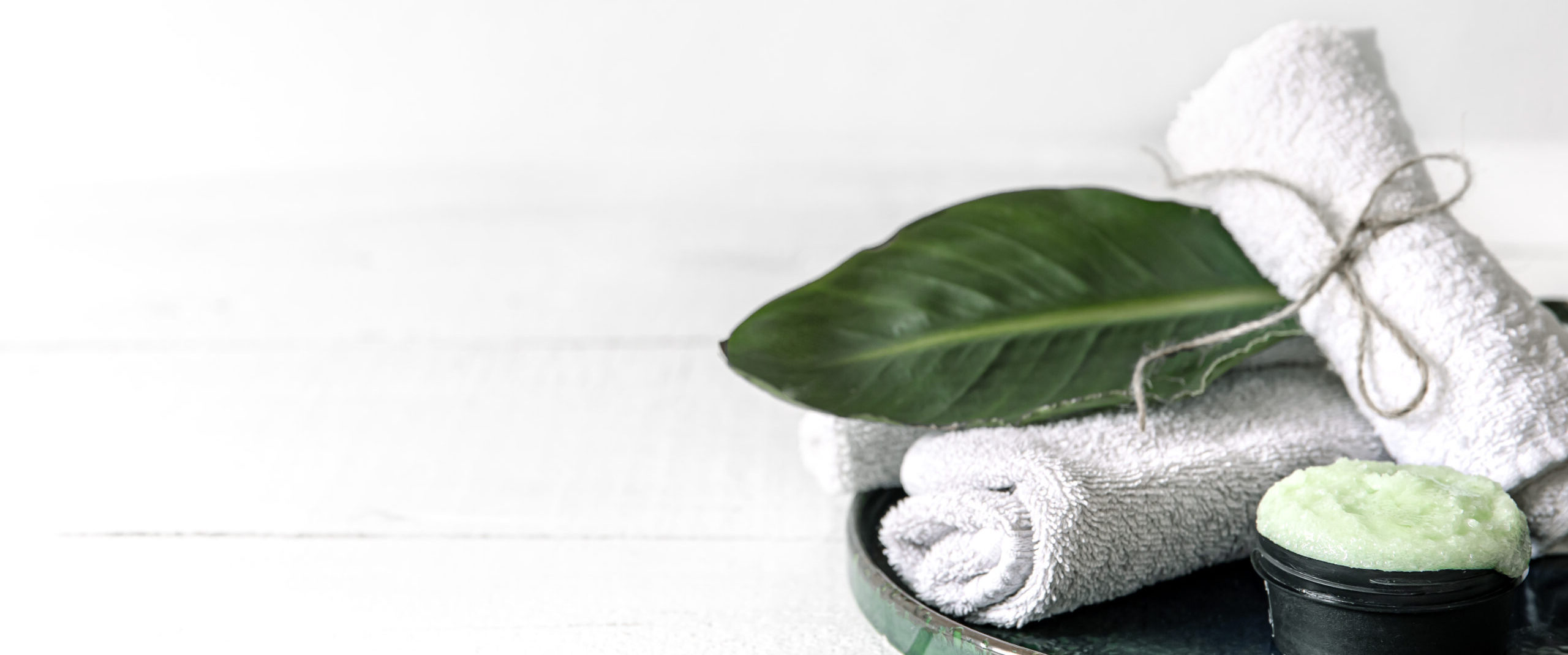 Spa composition with a natural care product with leaf and towels copy space.